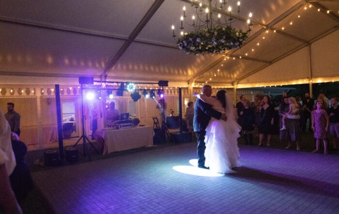 The bride and groom dancing under the chandelier and string lights of the wedding tent.