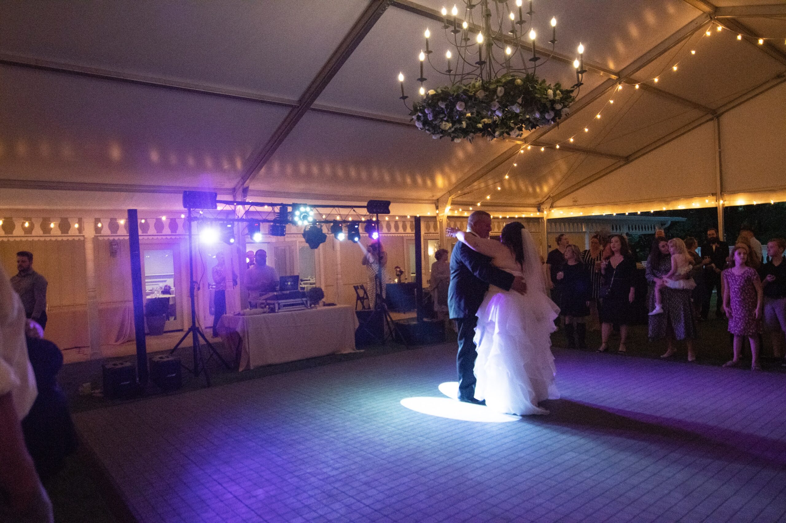 The bride and groom dancing under the chandelier and string lights of the wedding tent.