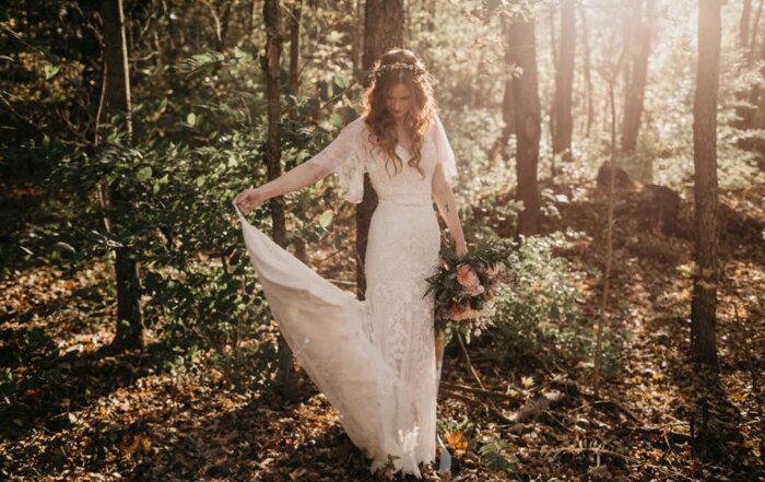 Boho bride in forest twirling her white wedding dress - she has curly hair and the sun is behind her