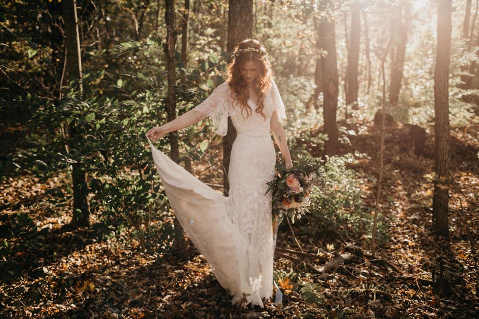 Boho bride in forest twirling her white wedding dress - she has curly hair and the sun is behind her