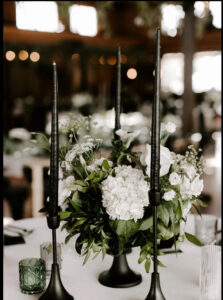 In season white flowers with dark olive greenery surrounded by black tapper candles